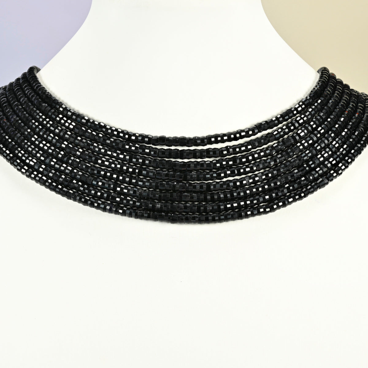 Black onyx faceted heishi disc strands arranged as a layered collar on a white display bust, black beads across the neck