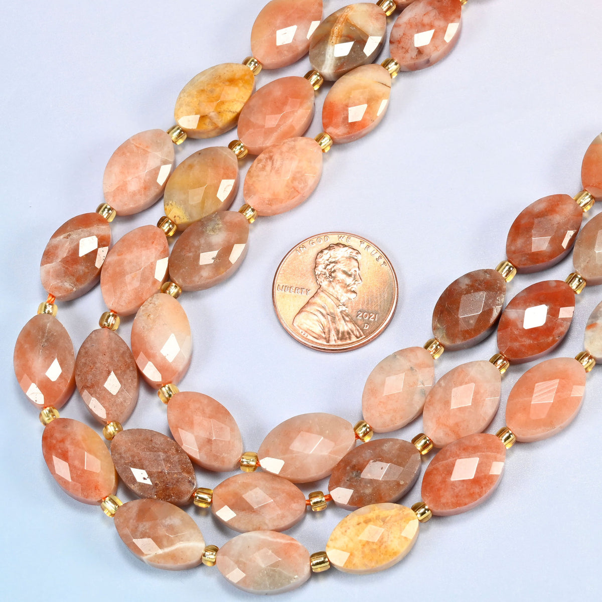 Close view of red crazy agate faceted flat oval strands curving beside a US penny for scale