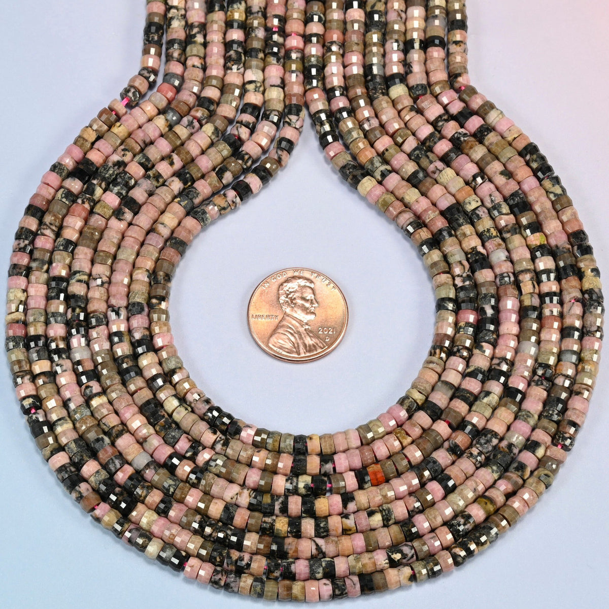 Rhodonite faceted heishi disc strands formed into a teardrop loop around a US penny for scale