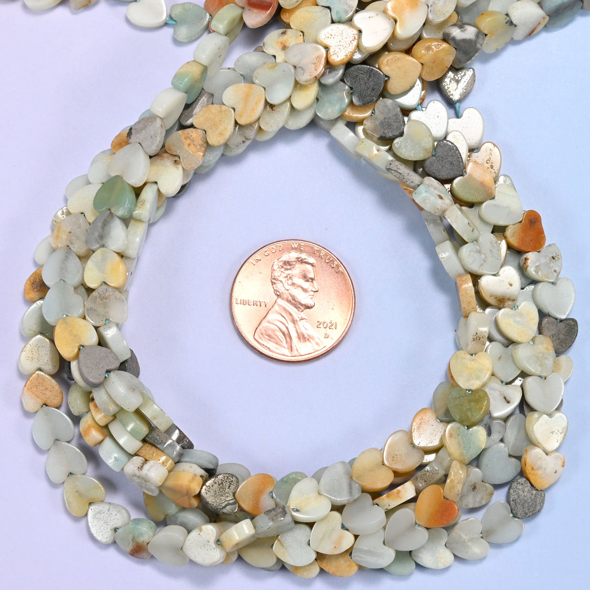 Multicolor Amazonite flat heart bead strands coiled around a US penny for size reference