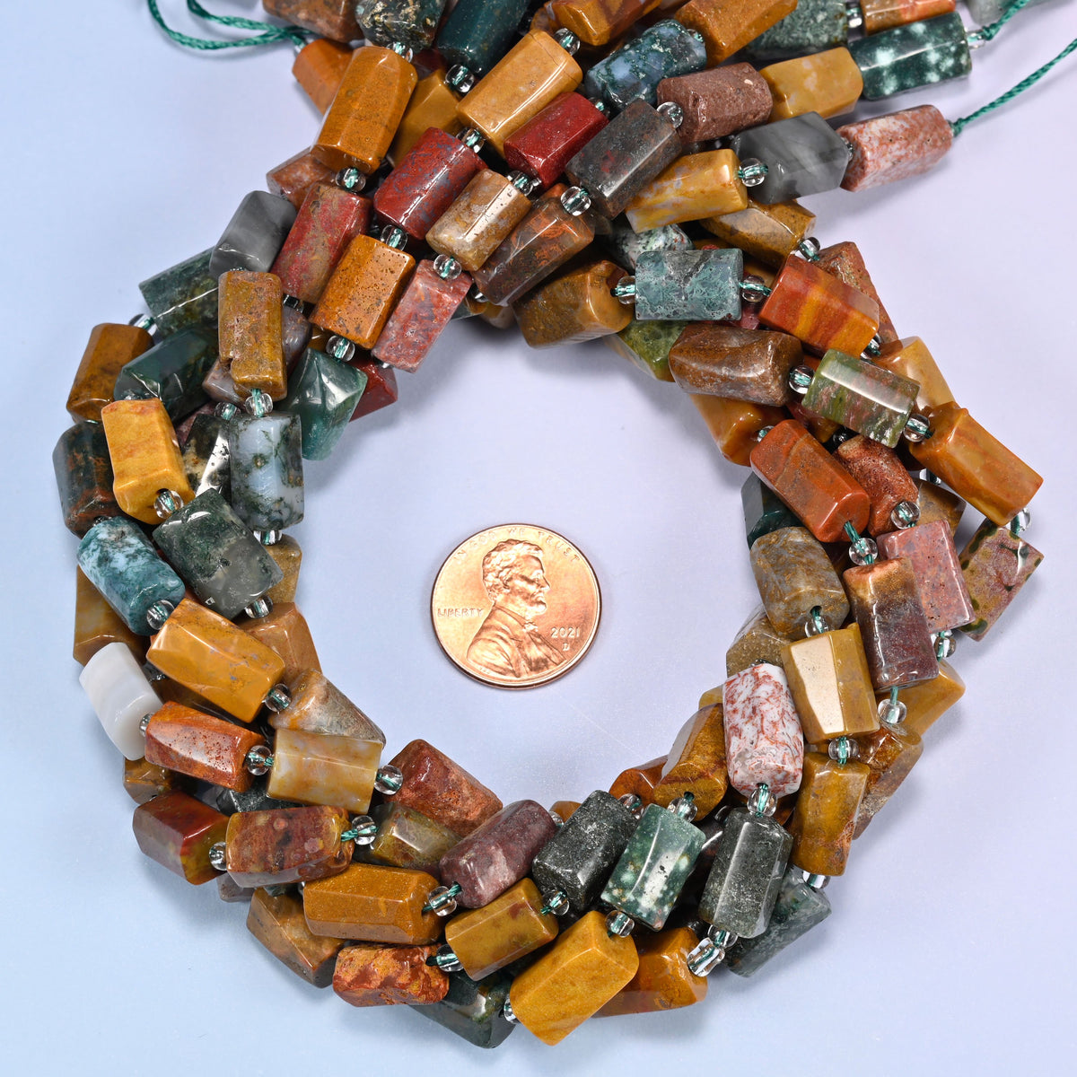 Ocean Jasper faceted tube bead strands coiled around a US penny for size reference
