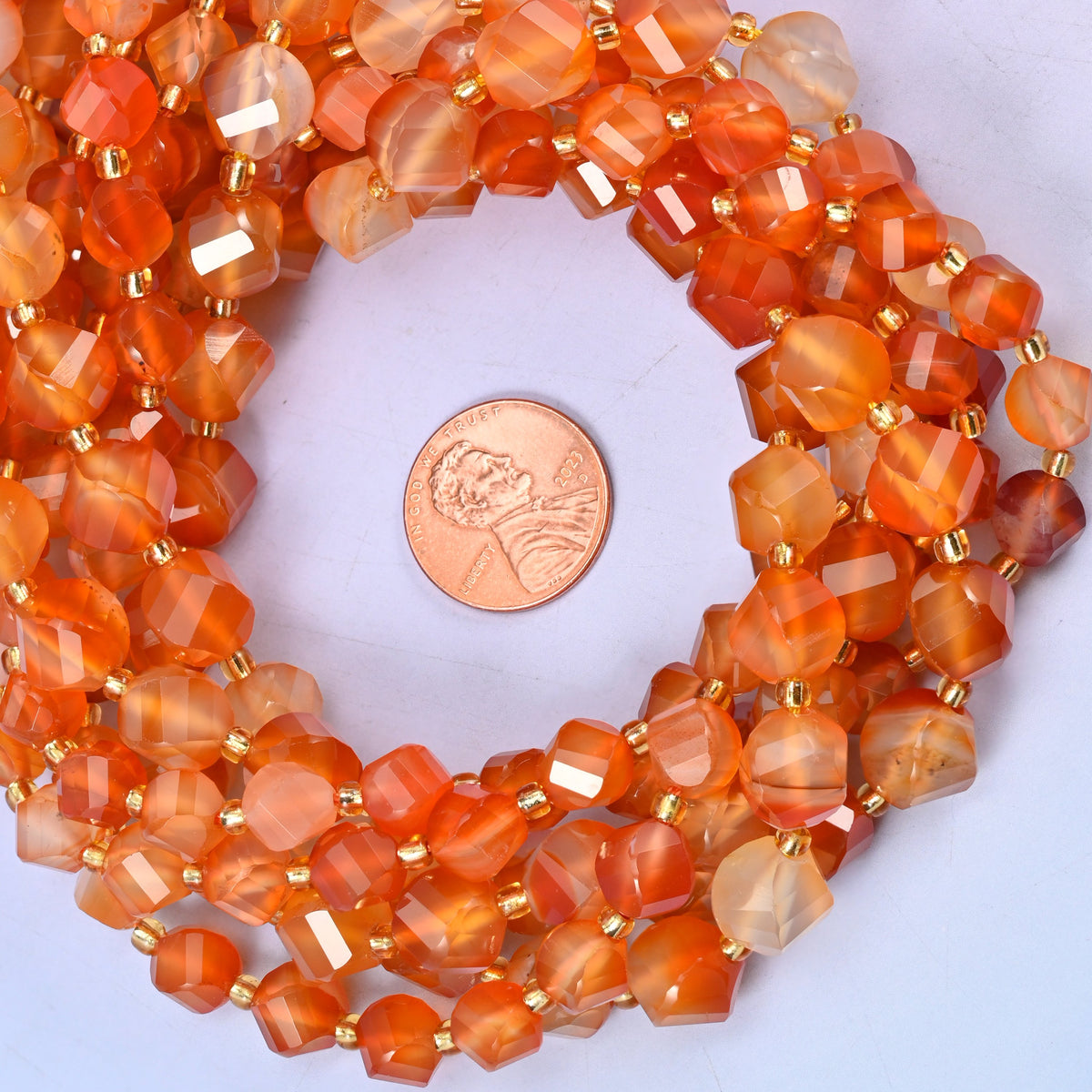 Orange Carnelian faceted spiral twist bead strands coiled around a US penny for size reference