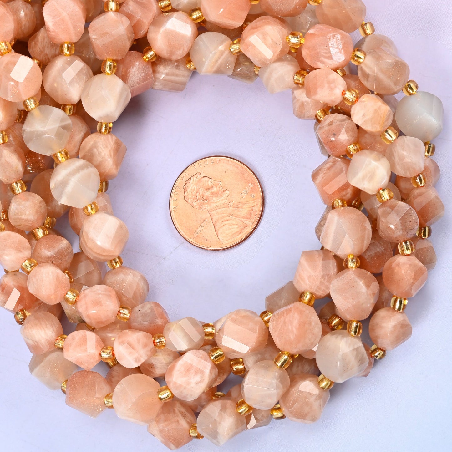 Orange Sunstone faceted spiral twist bead strands coiled around a US penny for size reference