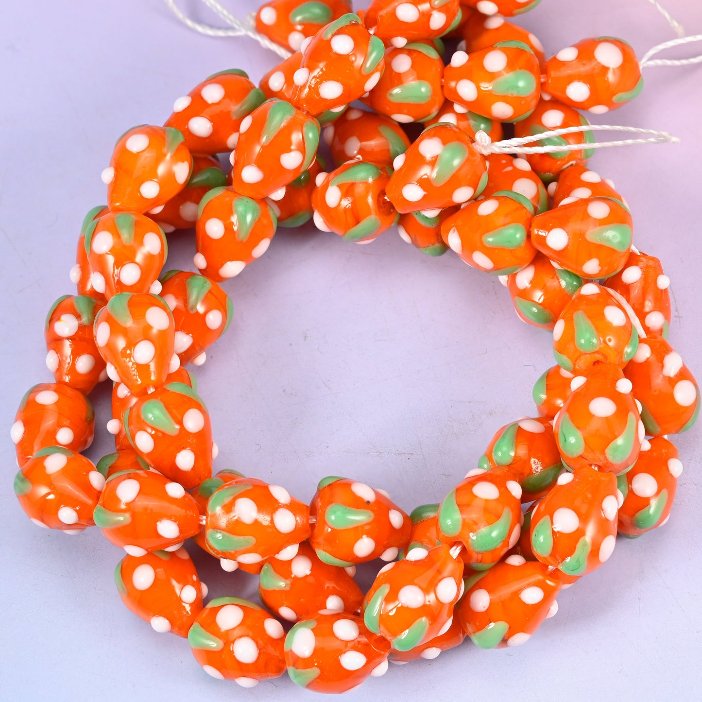 Orange White Dots Strawberry glass beads, close view of the coiled strands in orange with green leaves and white seed dots