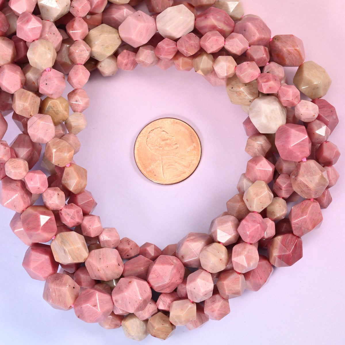 Pink Rhodonite faceted diamond star cut bead strands coiled around a US penny for size reference