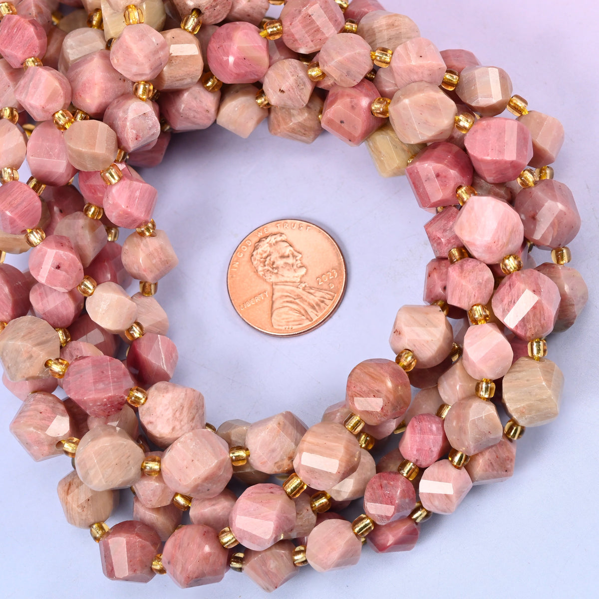 Pink Rhodonite faceted spiral twist bead strands coiled around a US penny for size reference