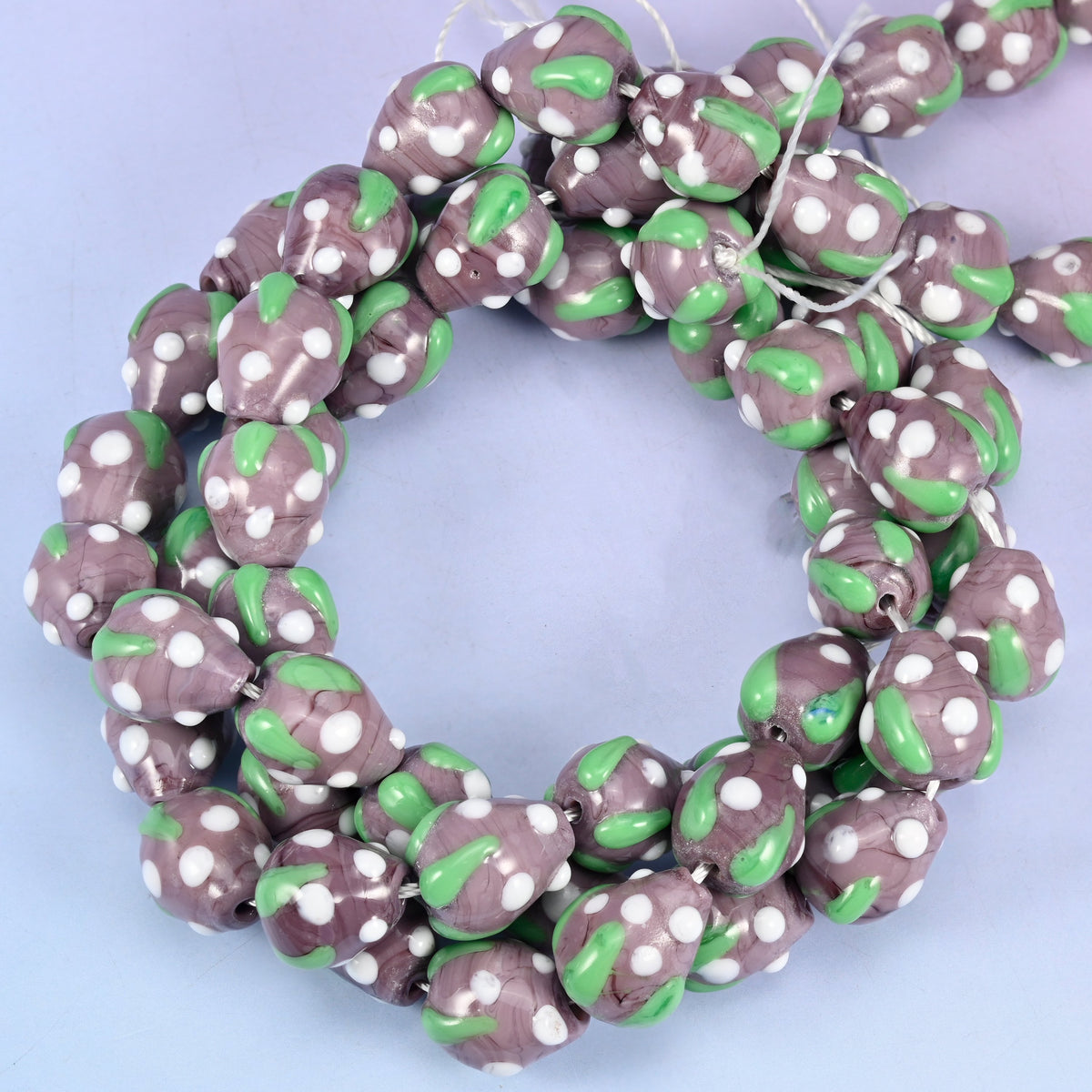 Purple White Dots Strawberry glass beads, close view of the coiled strands in dusty purple with green leaf panels and white seed dots