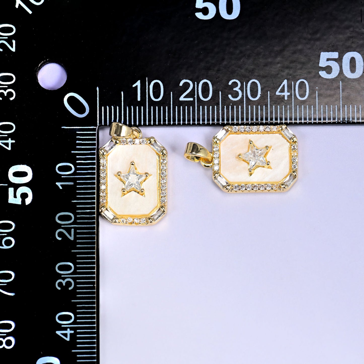 Two rectangle star charms with cream enamel and clear pave stones in a gold frame, shown front and angled, beside a millimetre ruler for scale
