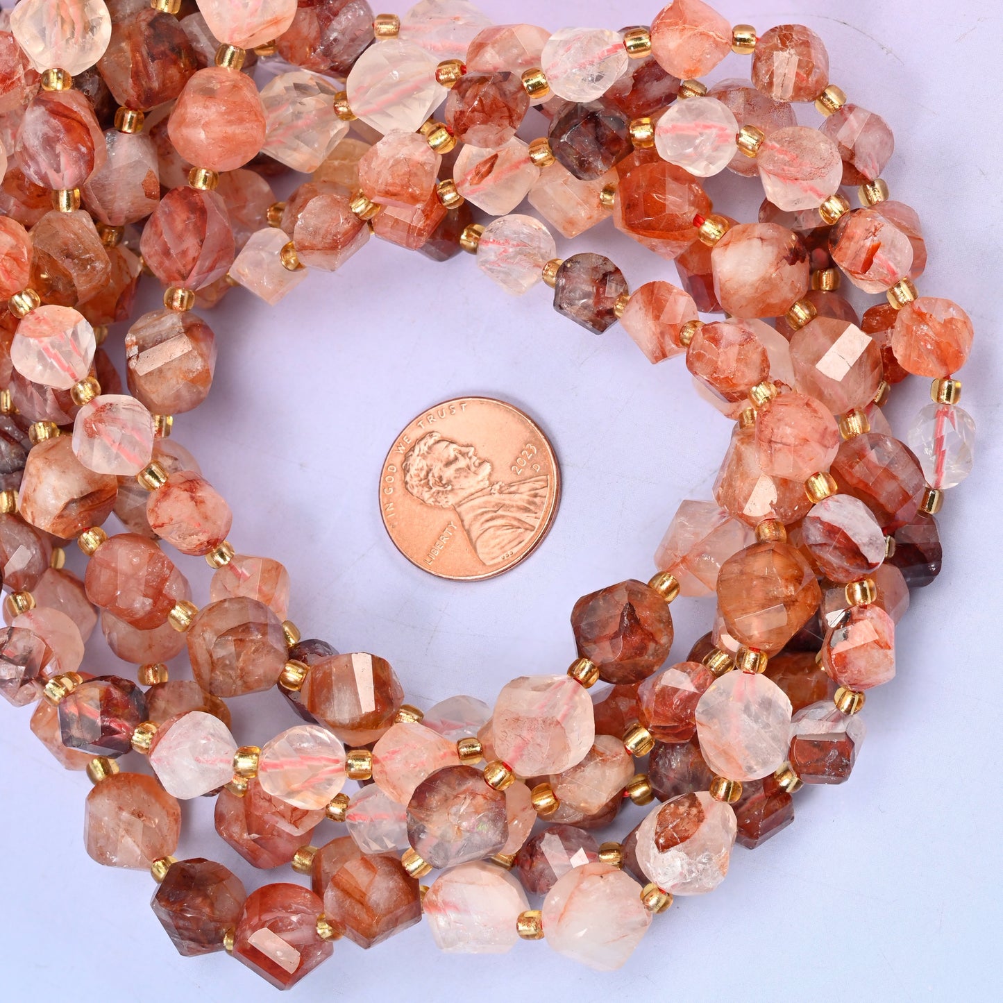 Red Hematoid Quartz faceted spiral twist bead strands coiled around a US penny for size reference