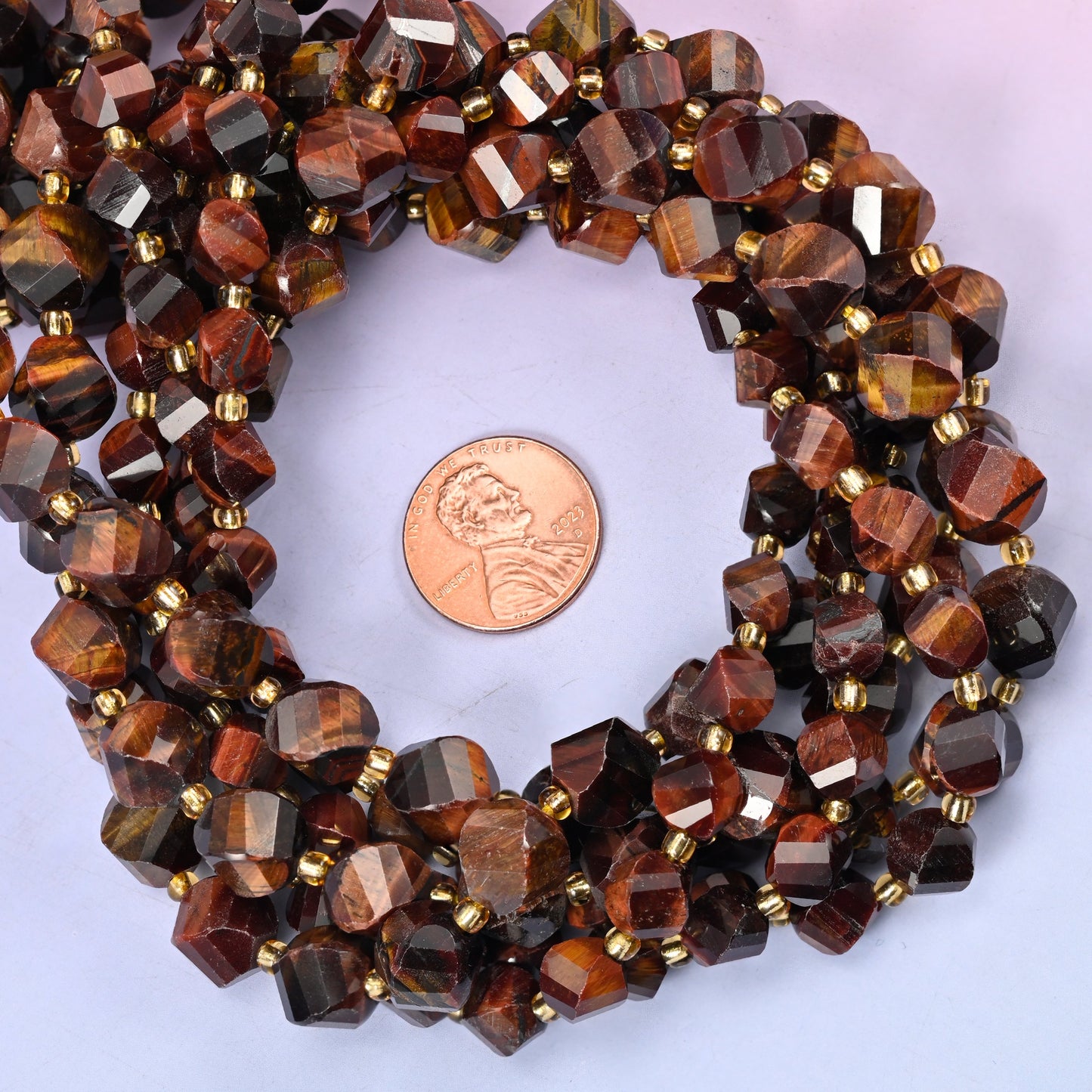 Red Tiger Eye faceted spiral twist bead strands coiled around a US penny for size reference