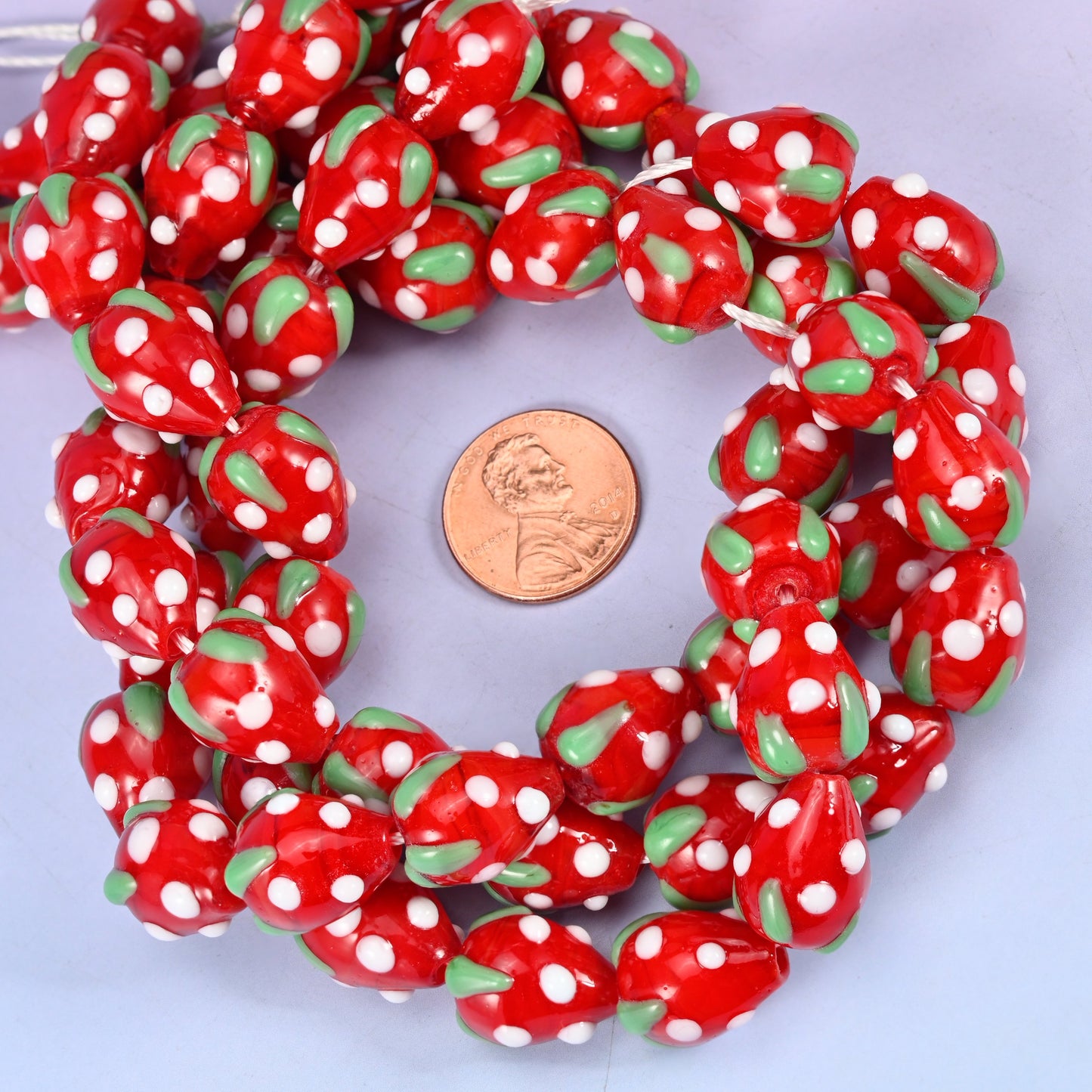 Red White Dots Strawberry glass bead strands coiled around a US penny for size reference