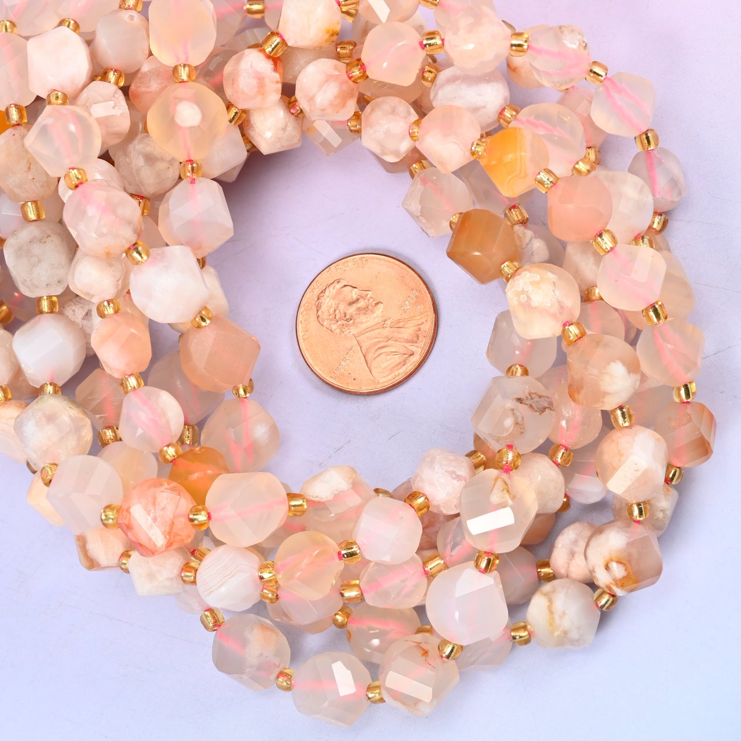 Sakura Flower Agate faceted spiral twist bead strands coiled around a US penny for size reference