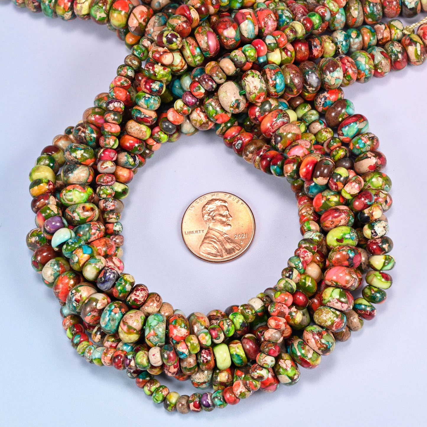Dyed Sea Sediment Jasper rondelle bead strands coiled around a US penny for size reference