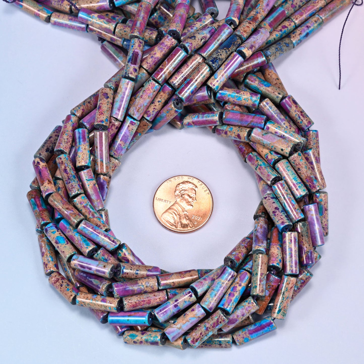 Sea Sediment Jasper tube bead strands coiled around a US penny for size reference