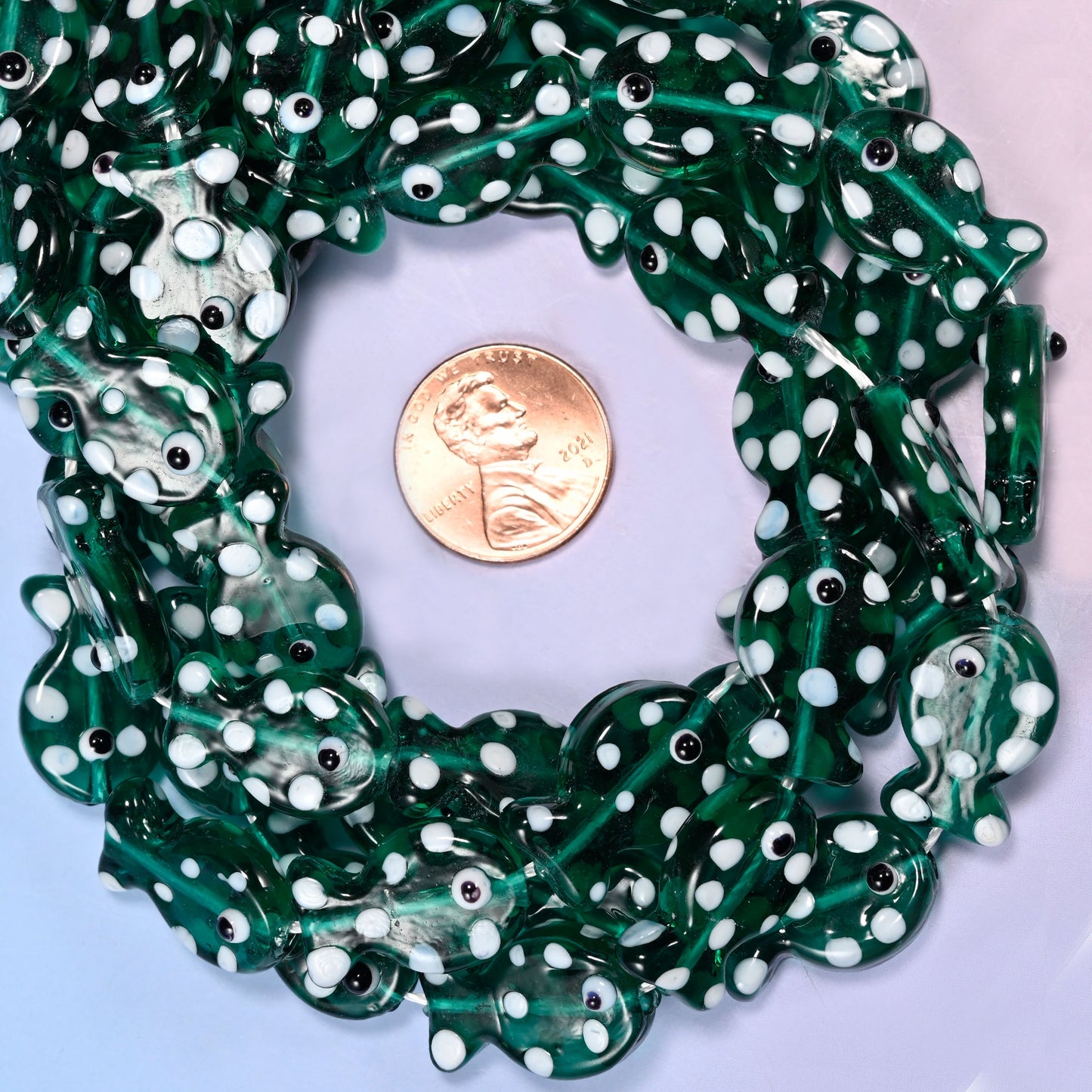 Transparent Jungle Green Fish glass bead strands coiled around a US penny for size reference