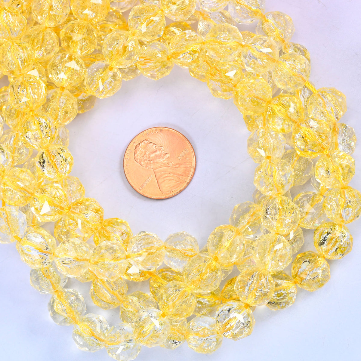 Transparent yellow faceted round glass bead strands coiled around a US penny for size reference