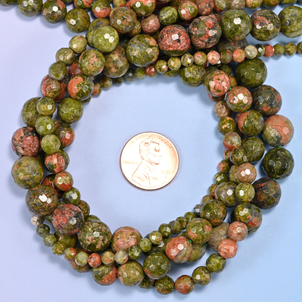 Unakite faceted round bead strands coiled around a US penny for size reference