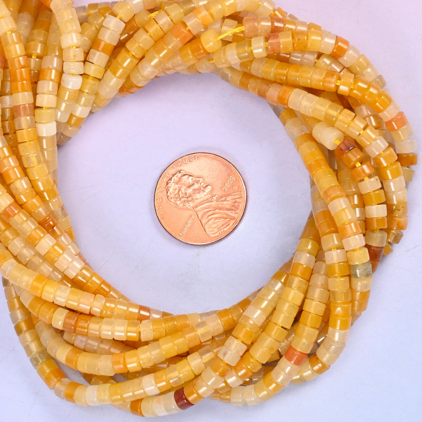 Yellow Jade smooth heishi disc bead strands coiled around a US penny for size reference