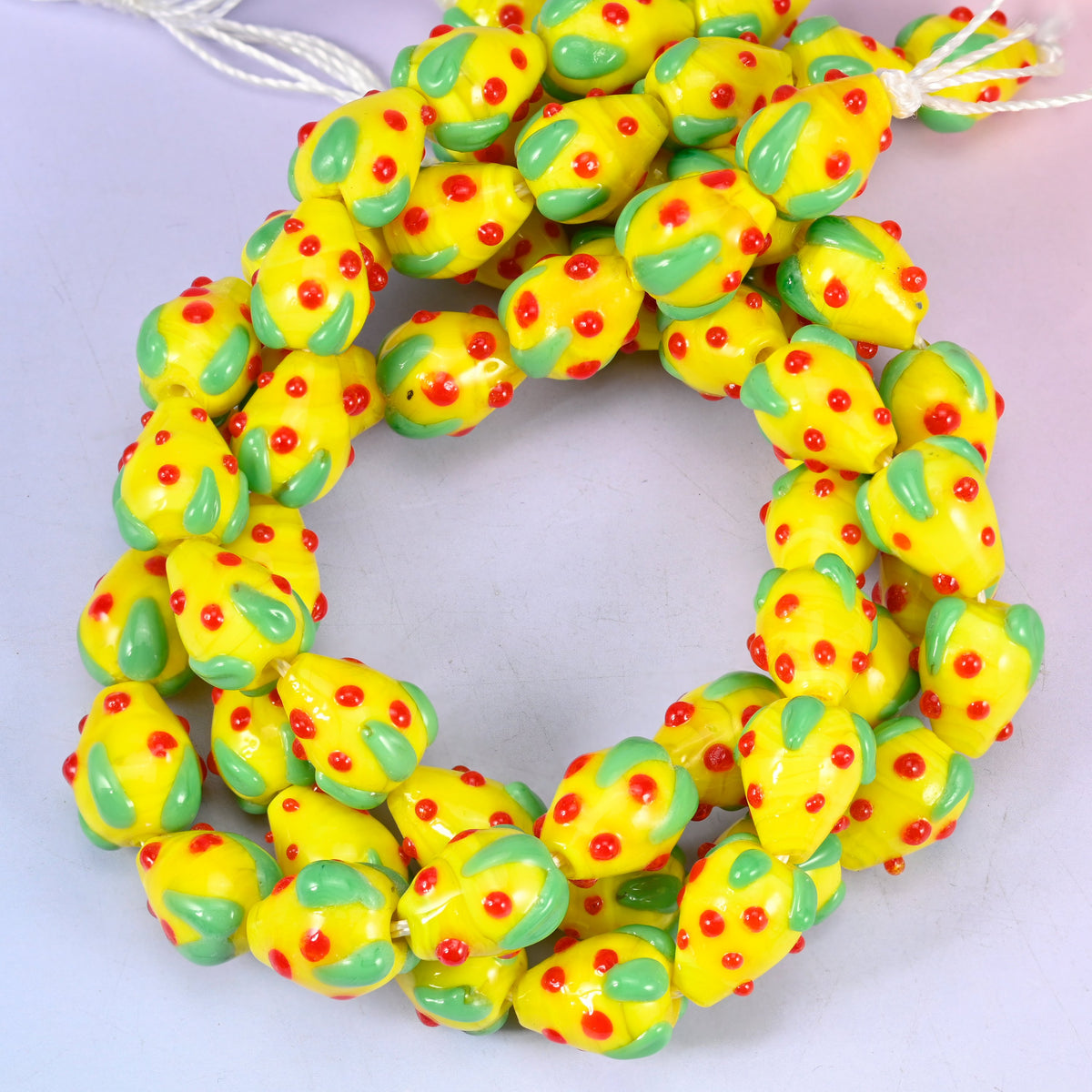 Yellow Red Dots Strawberry glass beads, close view of the coiled strands in yellow with green leaf panels and red seed dots