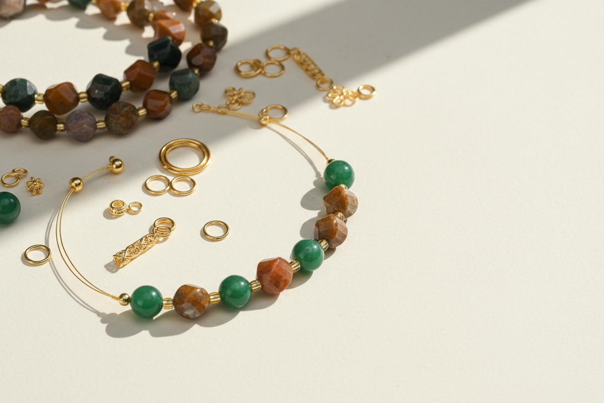 Green and earth-toned gemstone bead jewelry laid out with gold jump rings, clasps and other findings