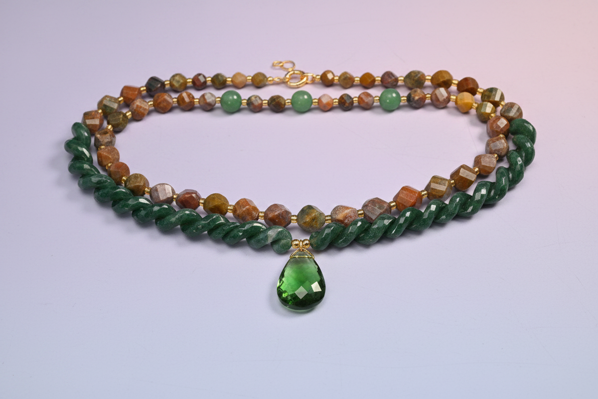 Layered necklace of green crystal beads with an earth-toned strand and a faceted green teardrop pendant