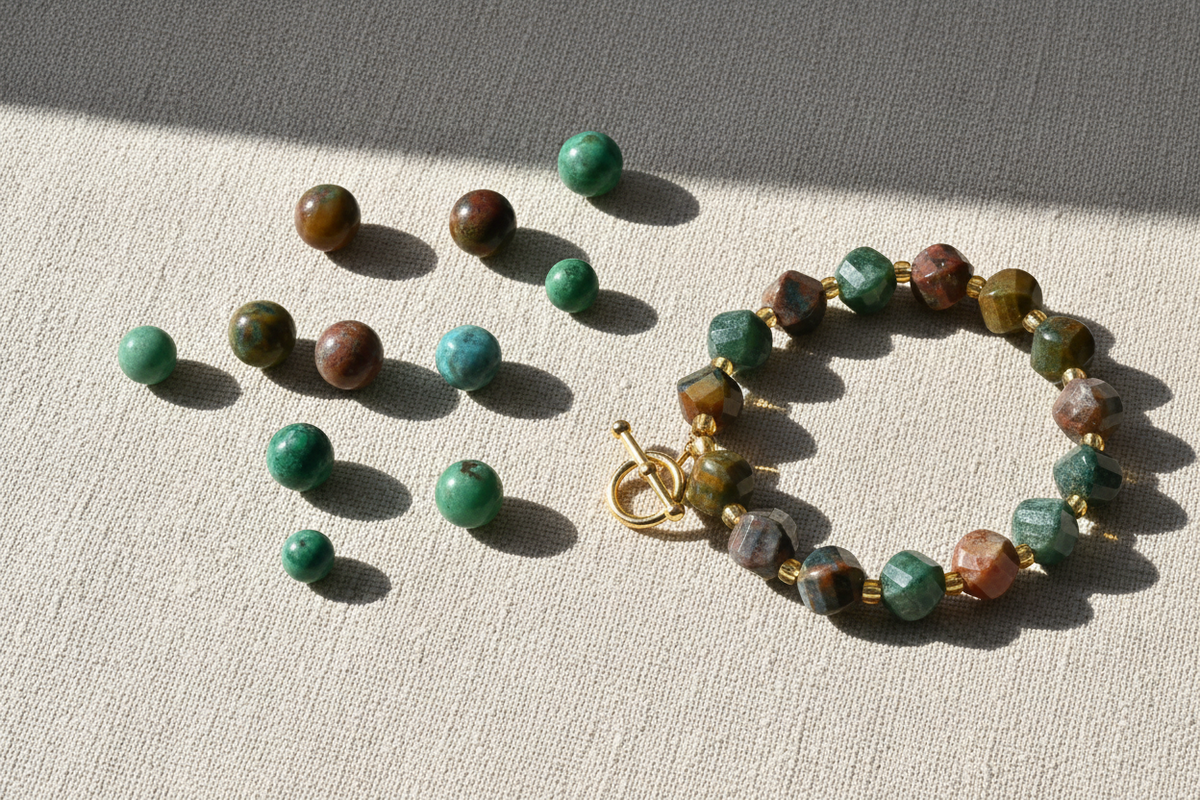 Loose round crystal beads in green and brown beside a finished bracelet with a gold toggle clasp