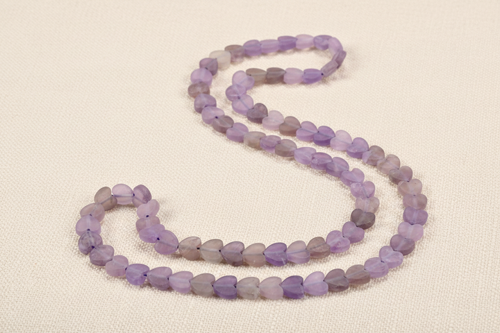 Matte lavender and purple amethyst heart beads with center holes arranged on ivory linen