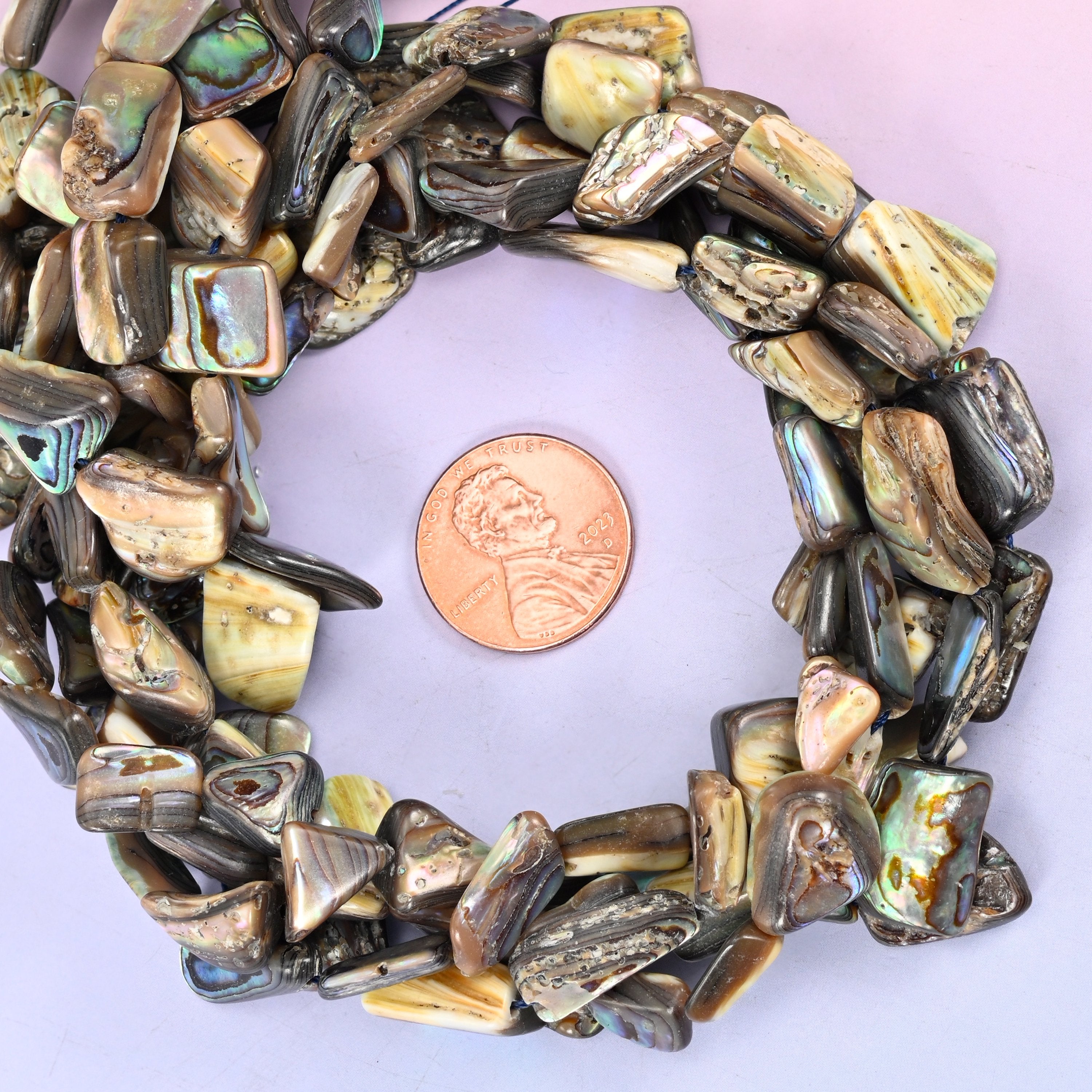 Abalone shell freeform bead strands coiled around a US penny for size reference