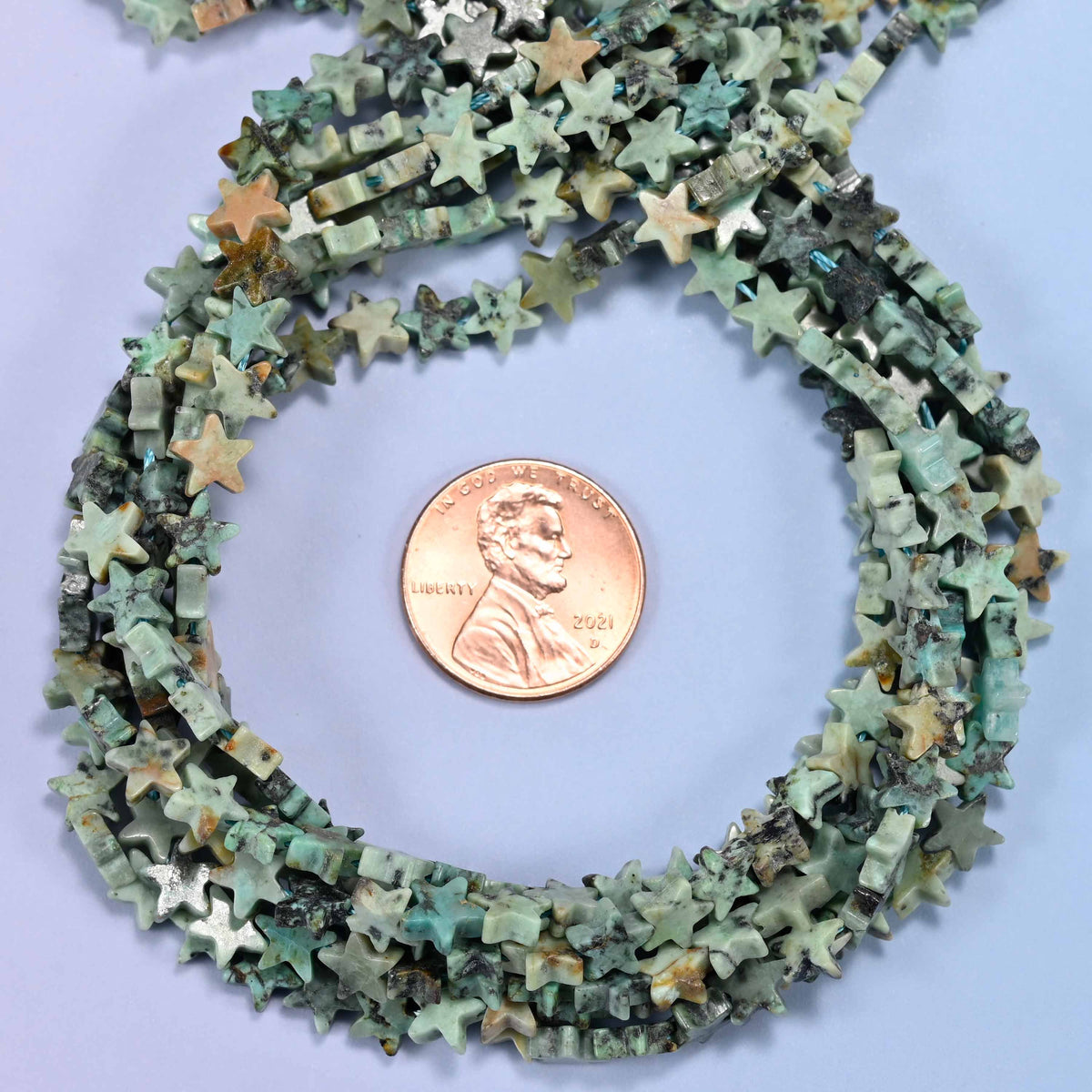 Natural African Howlite flat star bead strands coiled around a US penny for size reference