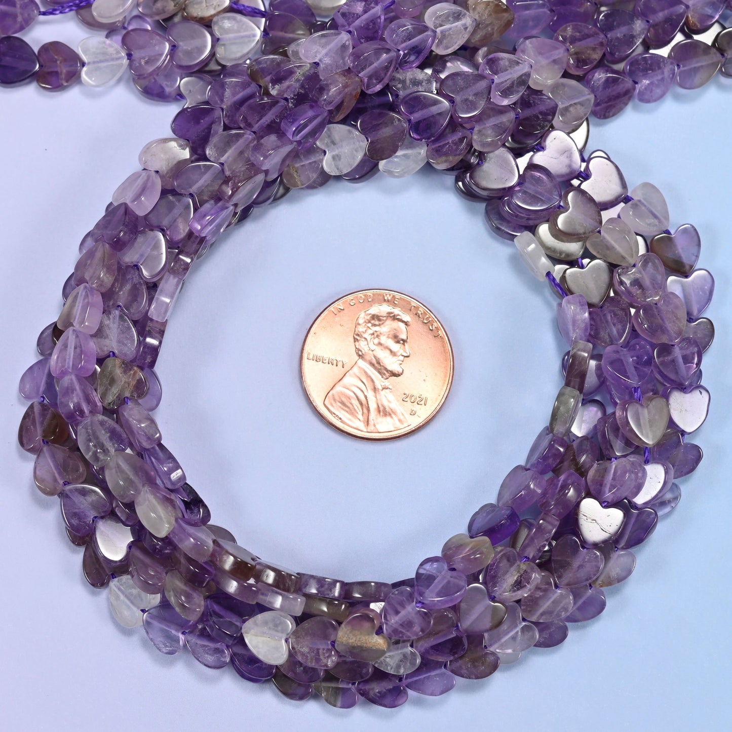 Amethyst flat heart bead strands coiled around a US penny for size reference