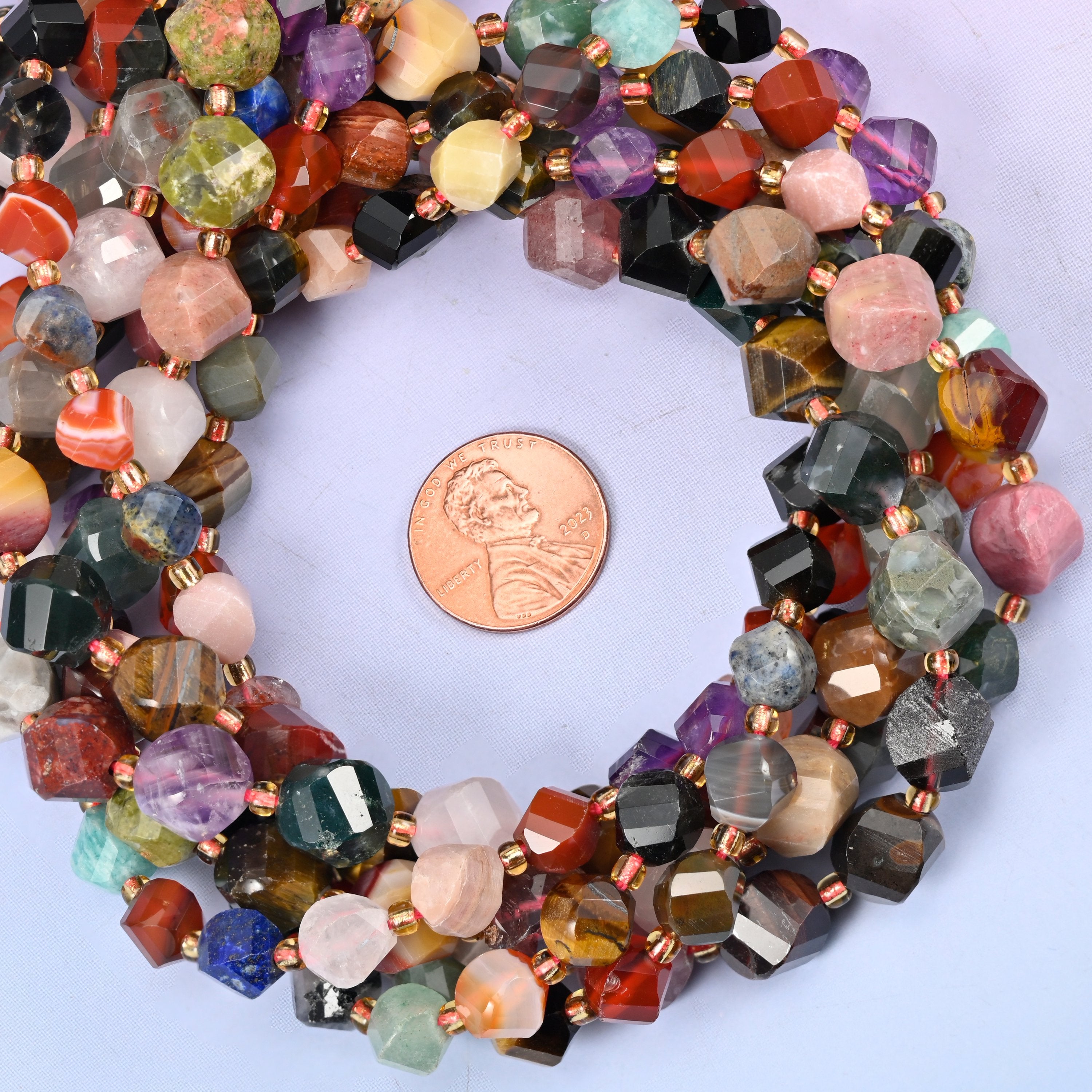 Assorted gemstone faceted spiral twist bead strands coiled around a US penny for size reference
