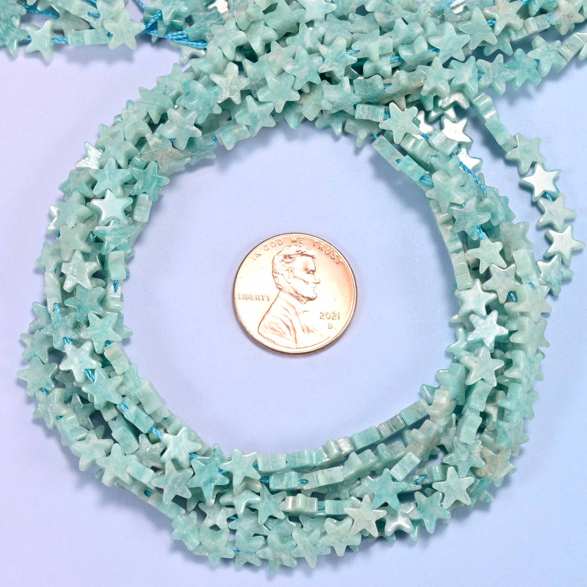 Blue Amazonite flat star bead strands coiled around a US penny for size reference