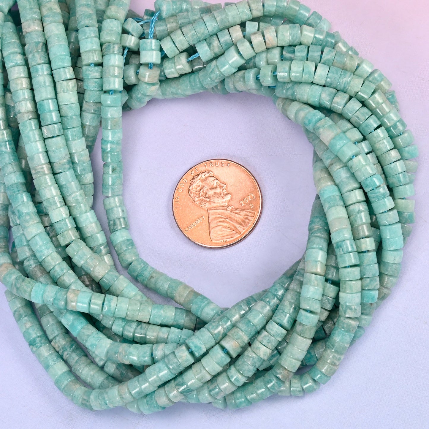 Blue Amazonite smooth heishi disc bead strands coiled around a US penny for size reference