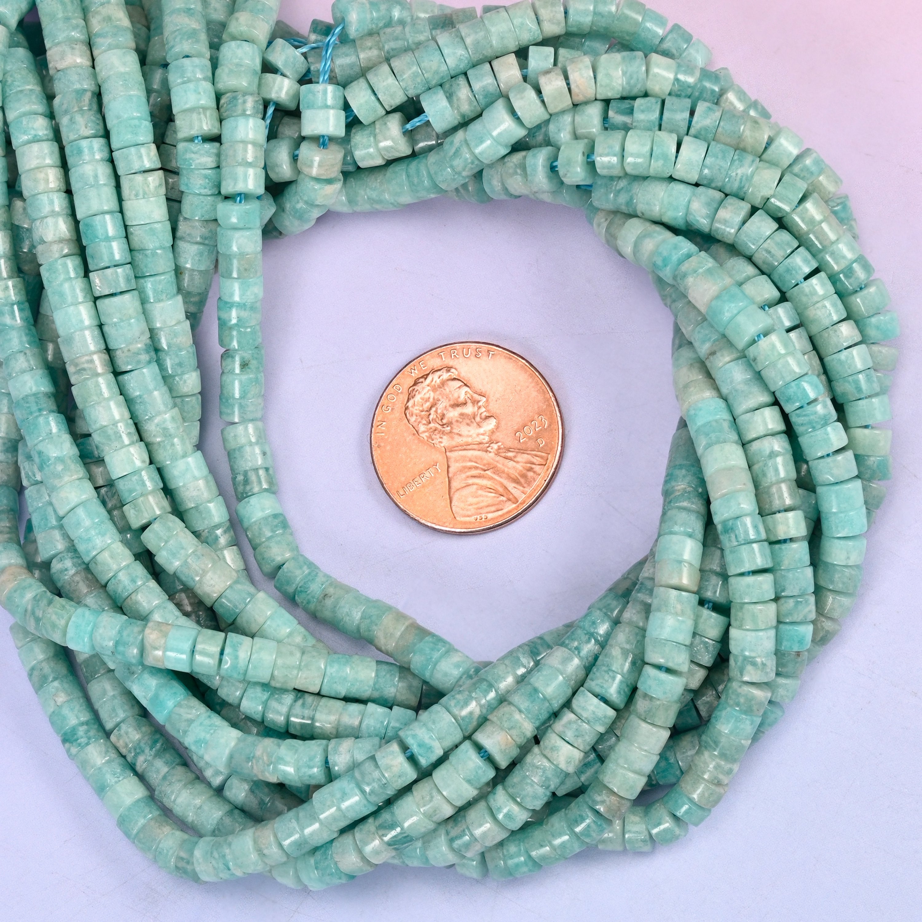 Blue Amazonite smooth heishi disc bead strands coiled around a US penny for size reference