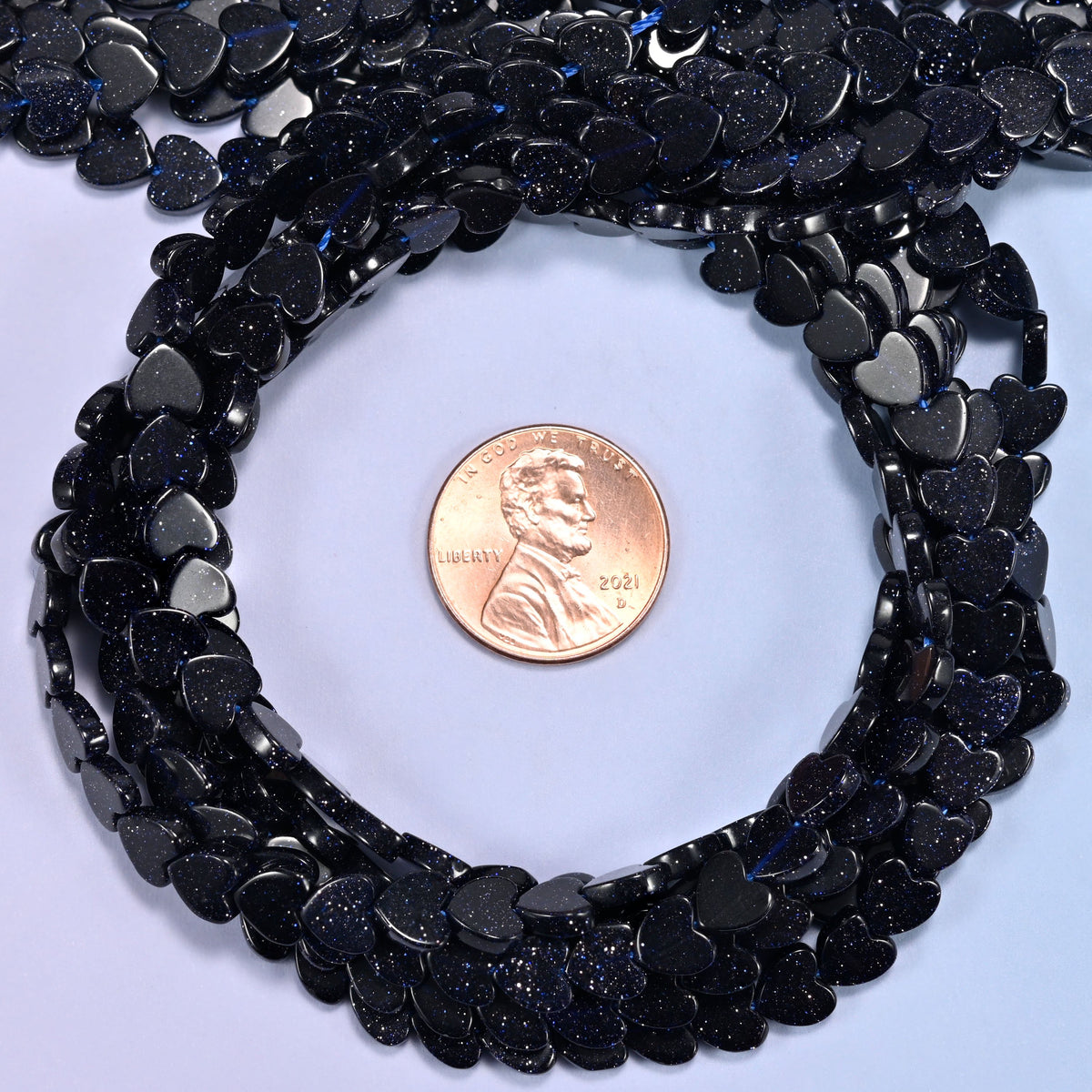 Blue Sandstone flat heart bead strands coiled around a US penny for size reference