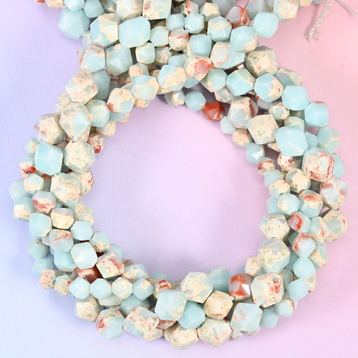 Blue Shoushan stone faceted diamond star cut beads, strands coiled into a ring showing the pale aqua stone with cream and rust markings
