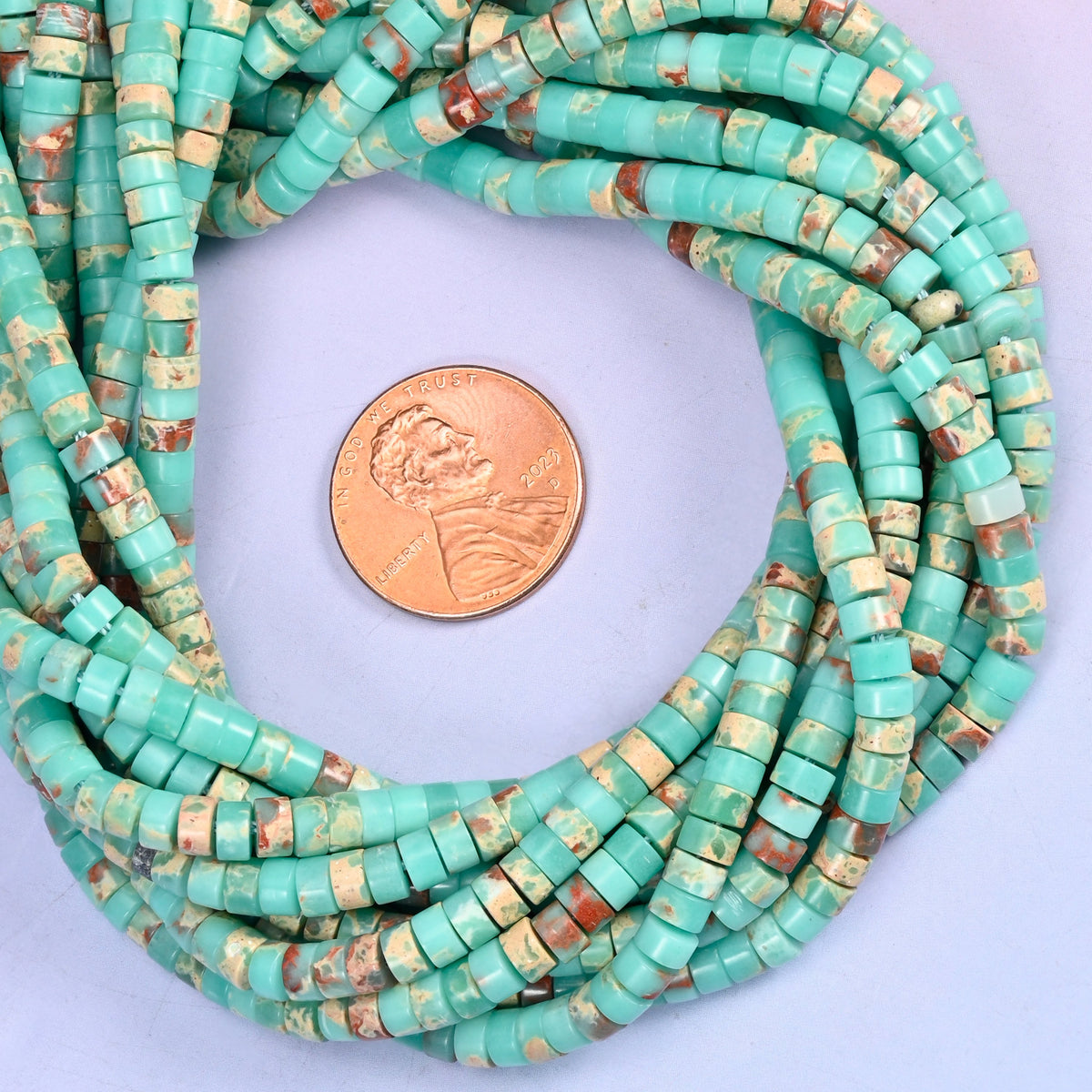 Blue Shoushan Stone smooth heishi disc bead strands coiled around a US penny for size reference