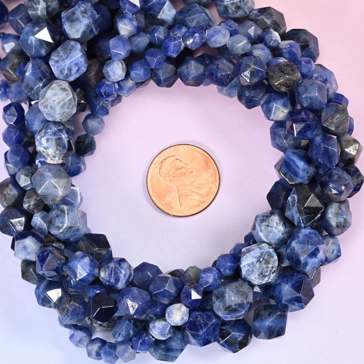 Blue sodalite diamond star cut beads coiled around a US penny for size reference.