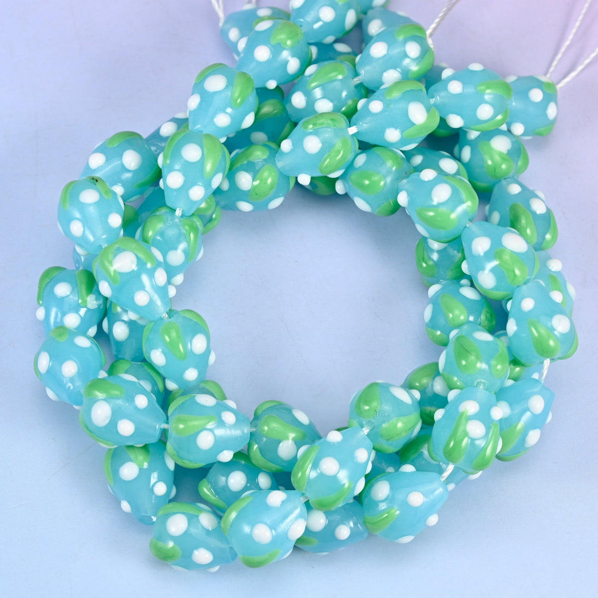 Blue White Dots Strawberry glass beads, close view of the coiled strands in pale blue with green leaves and white seed dots