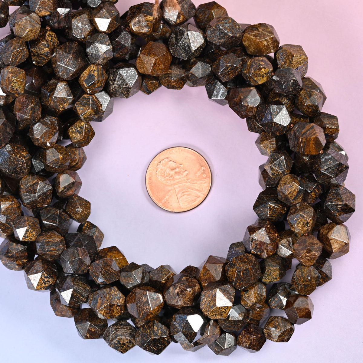 Bronzite faceted diamond star cut bead strands coiled around a US penny for size reference