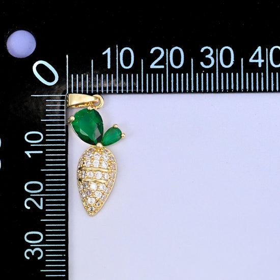 A carrot charm with a clear zircon body and green stone leaves, beside a millimetre ruler for scale
