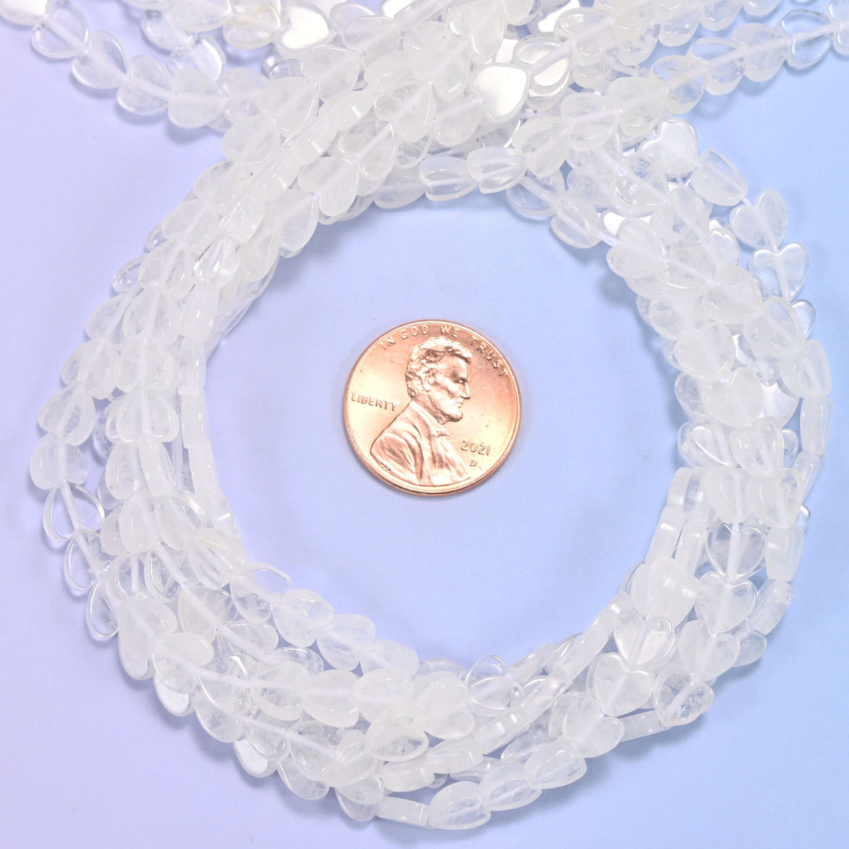 Clear Quartz flat heart bead strands coiled around a US penny for size reference