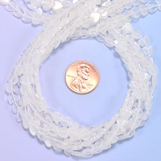 Clear Quartz flat heart bead strands coiled around a US penny for size reference