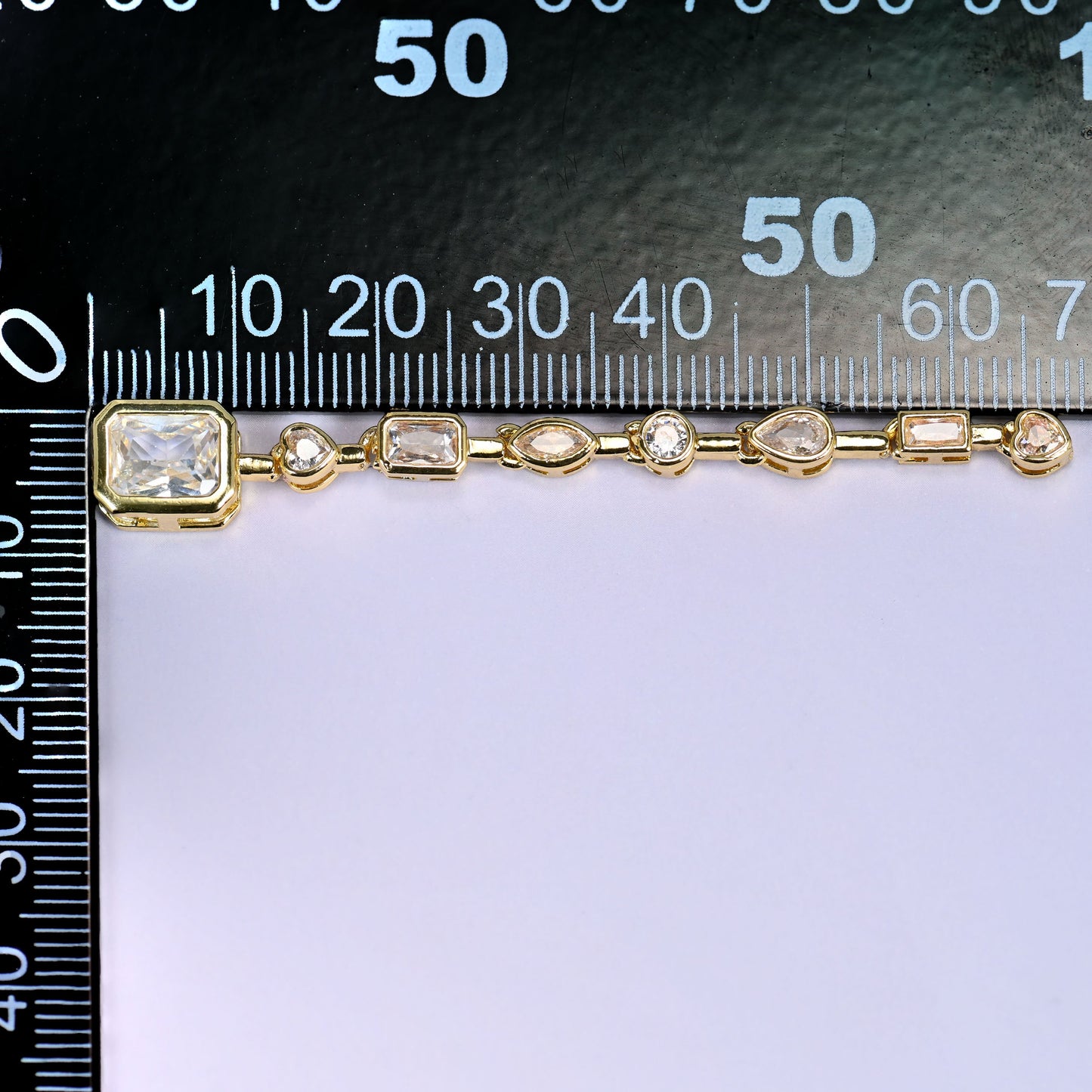 Clear rectangle pendant with a chain of small clear round and rectangular stones in gold, laid along a millimetre ruler for scale