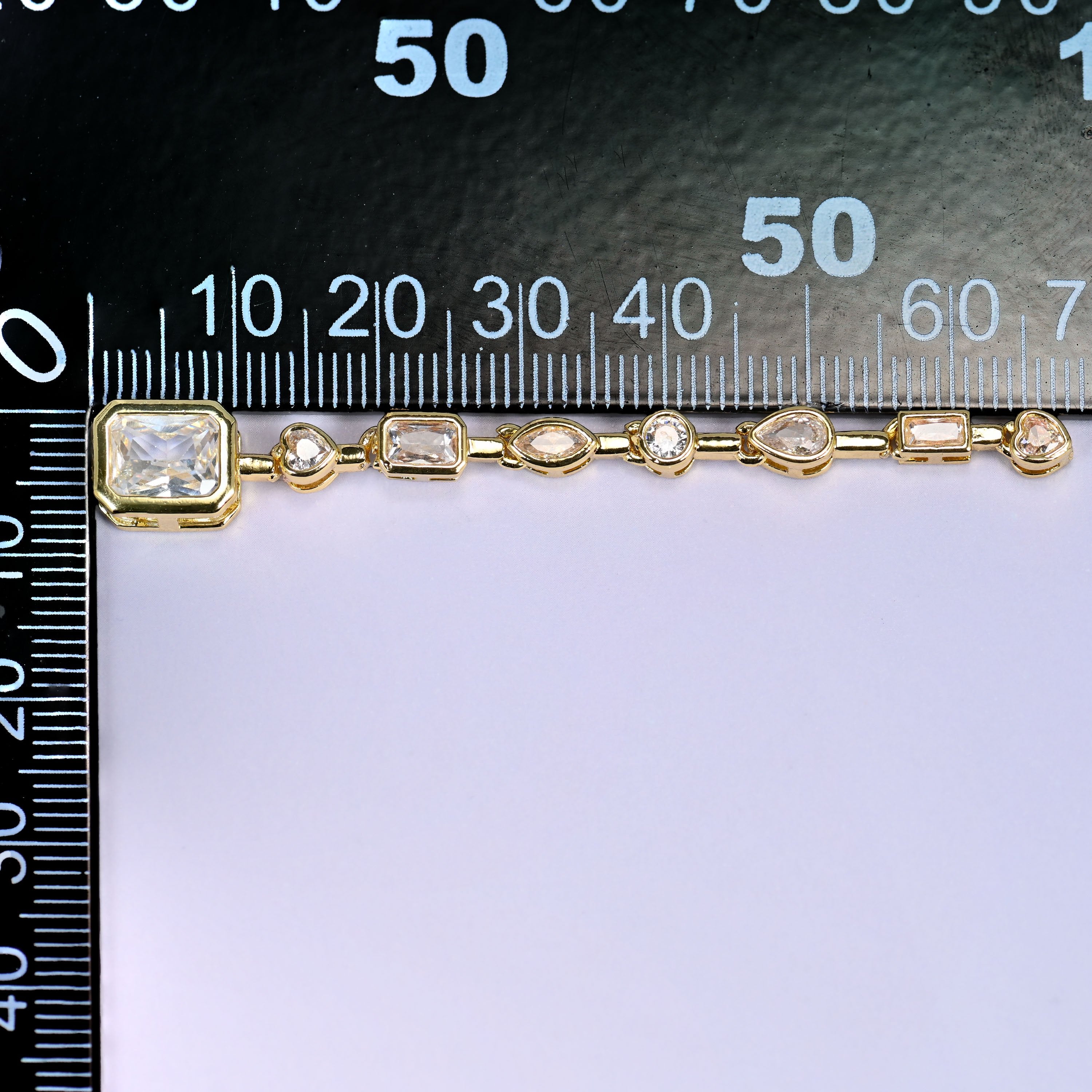 Clear rectangle pendant with a chain of small clear round and rectangular stones in gold, laid along a millimetre ruler for scale