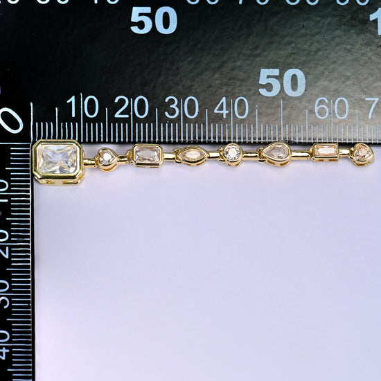Clear rectangle pendant with a chain of small clear round and rectangular stones in gold, laid along a millimetre ruler for scale