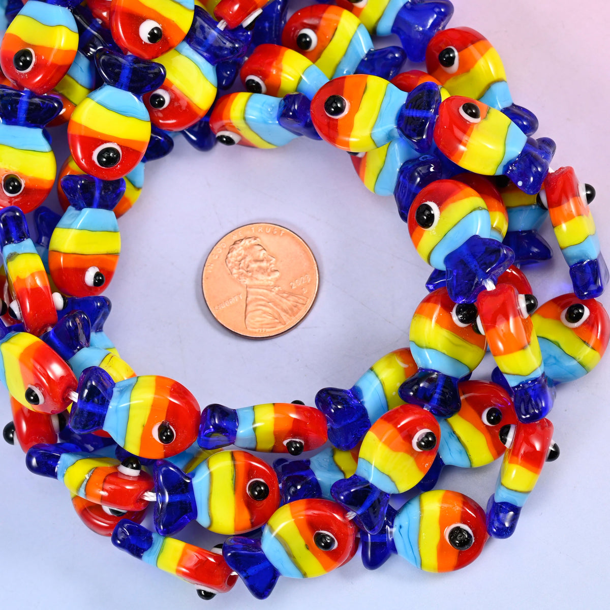 Colorful Fish glass bead strands coiled around a US penny for size reference