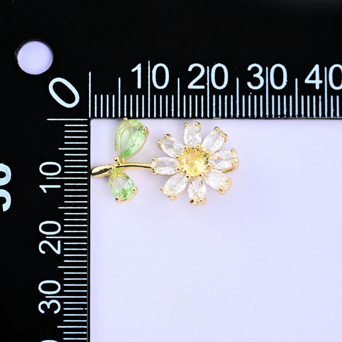 The daisy flower charm turned sideways beside a millimetre ruler for scale