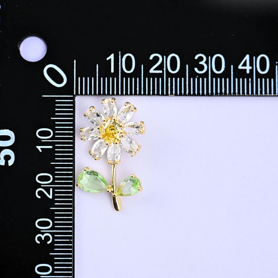 A daisy flower charm with clear petals, a yellow centre and green leaves, upright beside a millimetre ruler for scale