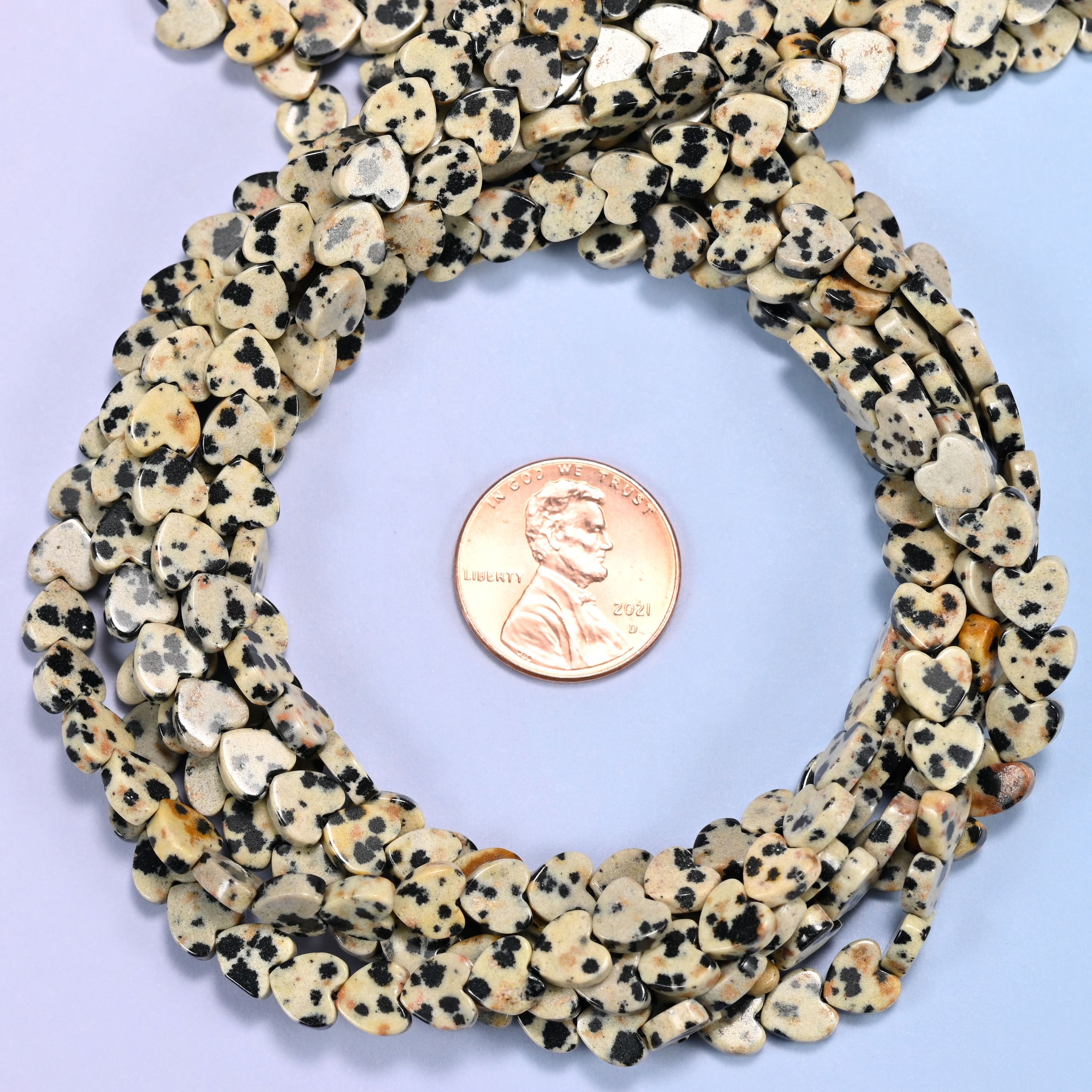 Dalmatian Jasper flat heart bead strands coiled around a US penny for size reference